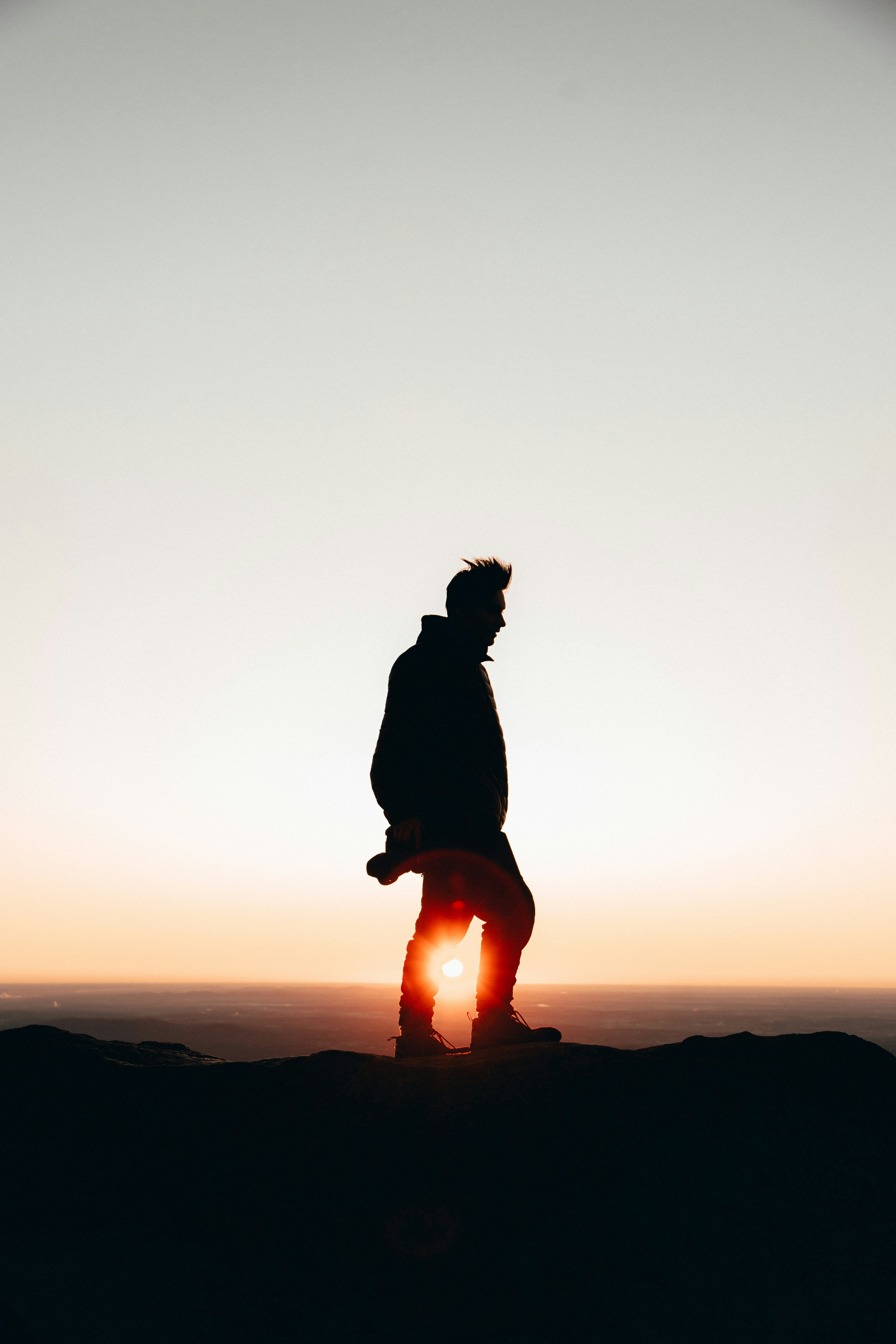 silhouette of man standing on cliff during golden hour